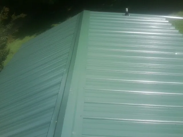 New green metal panels meeting at the ridge of a roof — Flat Roof Repair work by our crew in Milledgeville