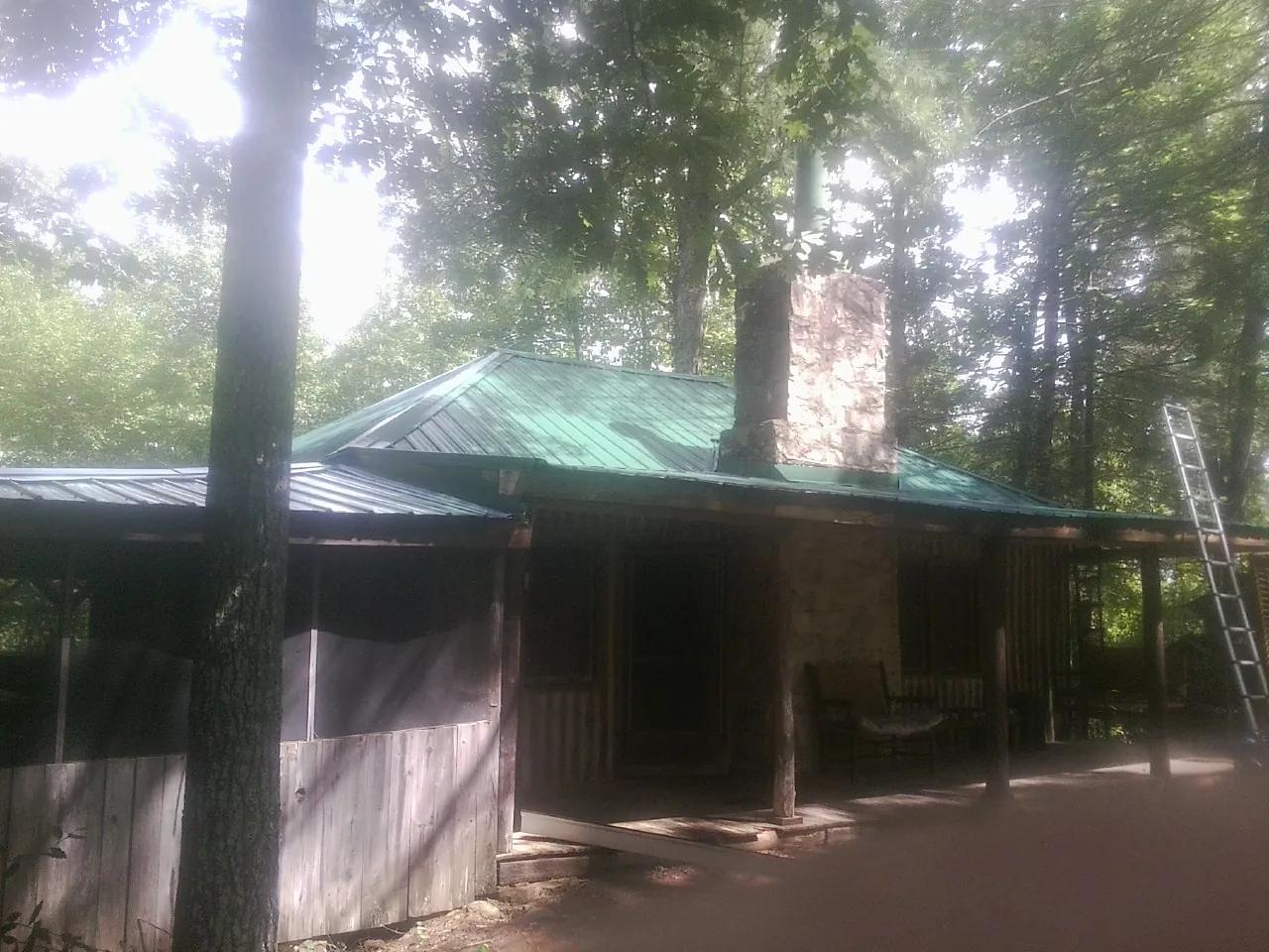 Green metal roof and stone chimney above a log cabin porch in Milledgeville